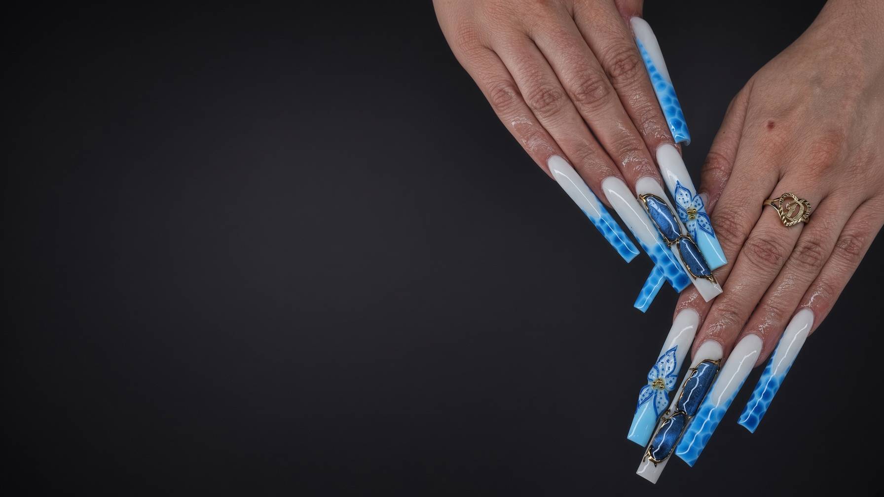 Hands with long square acrylic nails painted white and decorated with blue wave patterns wearing a gold ring against a dark background Nab nail bar | nails lashes and beauty in las vegas