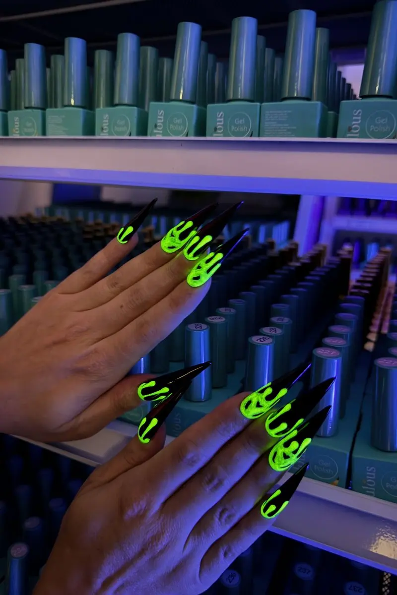 Glow in the dark halloween nails  neon green drip design on long black stiletto nails under blacklight at nab nail bar in las vegas nab nail bar