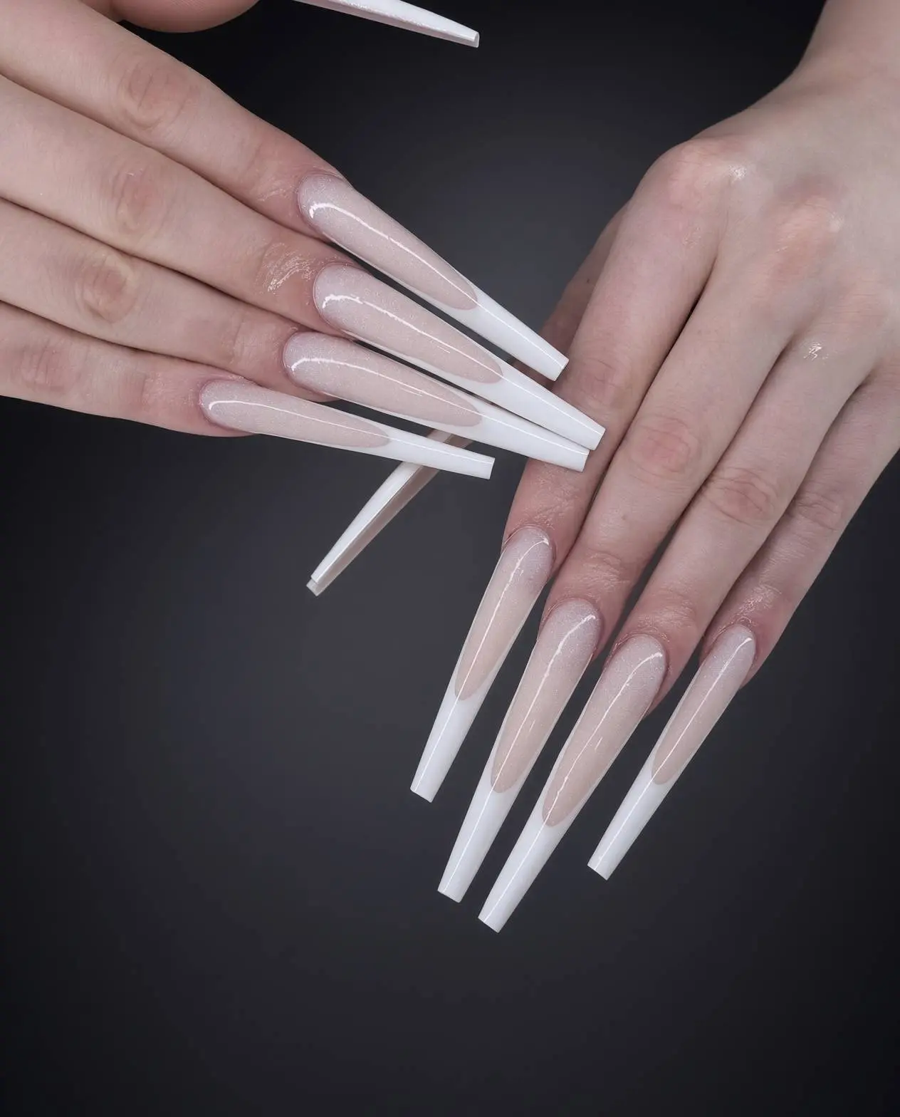 Close up of long coffin shaped acrylic nails with a nude base and white french tips on a dark background Nab nail bar