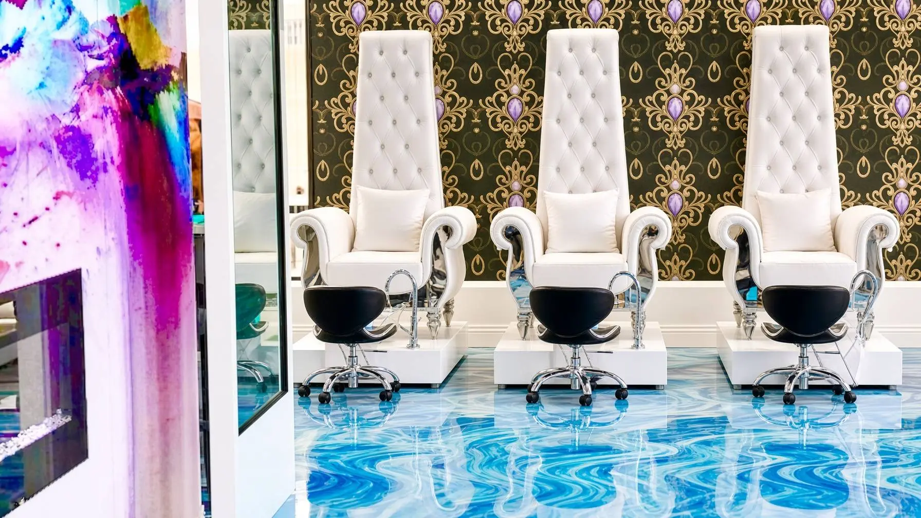 Row of tall white tufted salon chairs with white cushions against ornate gold and purple wallpaper Nab nail bar