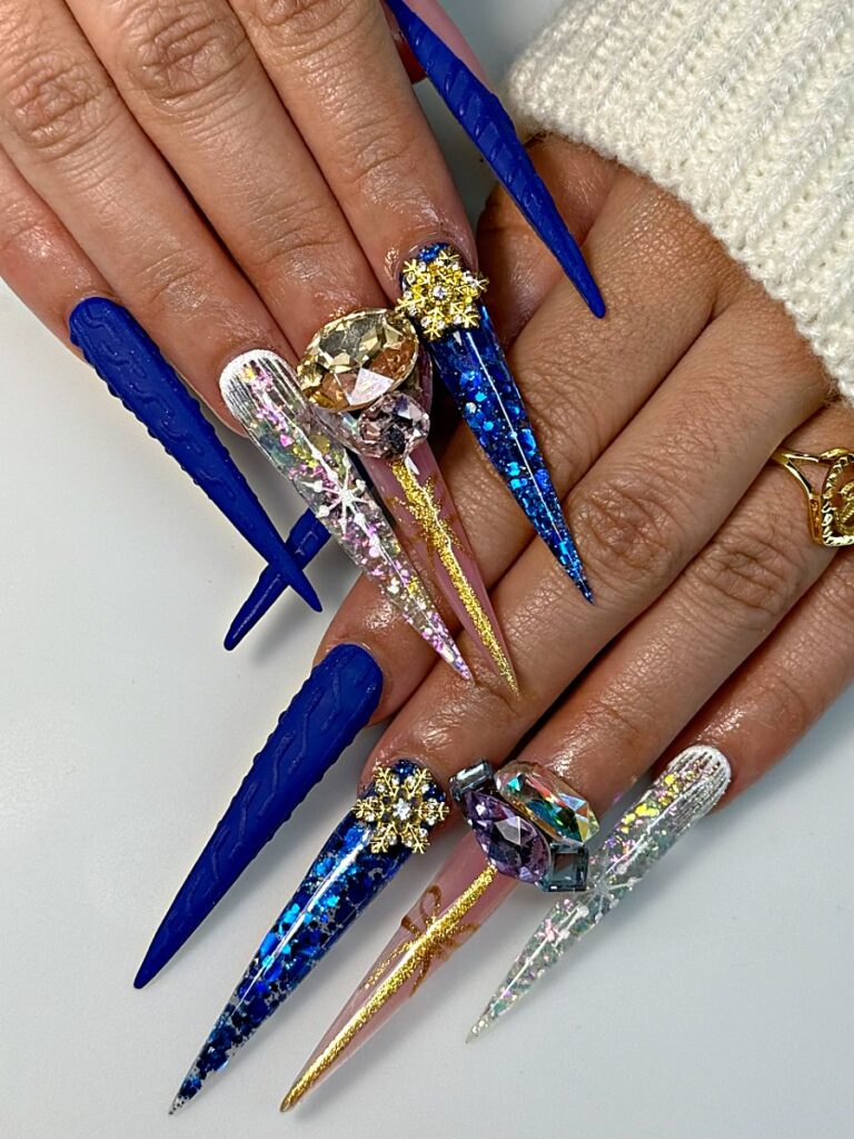 Royal blue winter stiletto nails with gold snowflake charms, crystals and glitter at NAB Nail Bar, Las Vegas