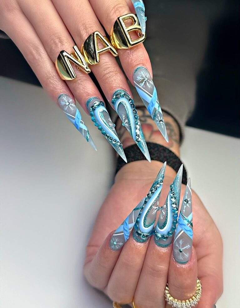 Long stiletto acrylic nails in icy blue with snowflake patterns, crystals, and teal beads.