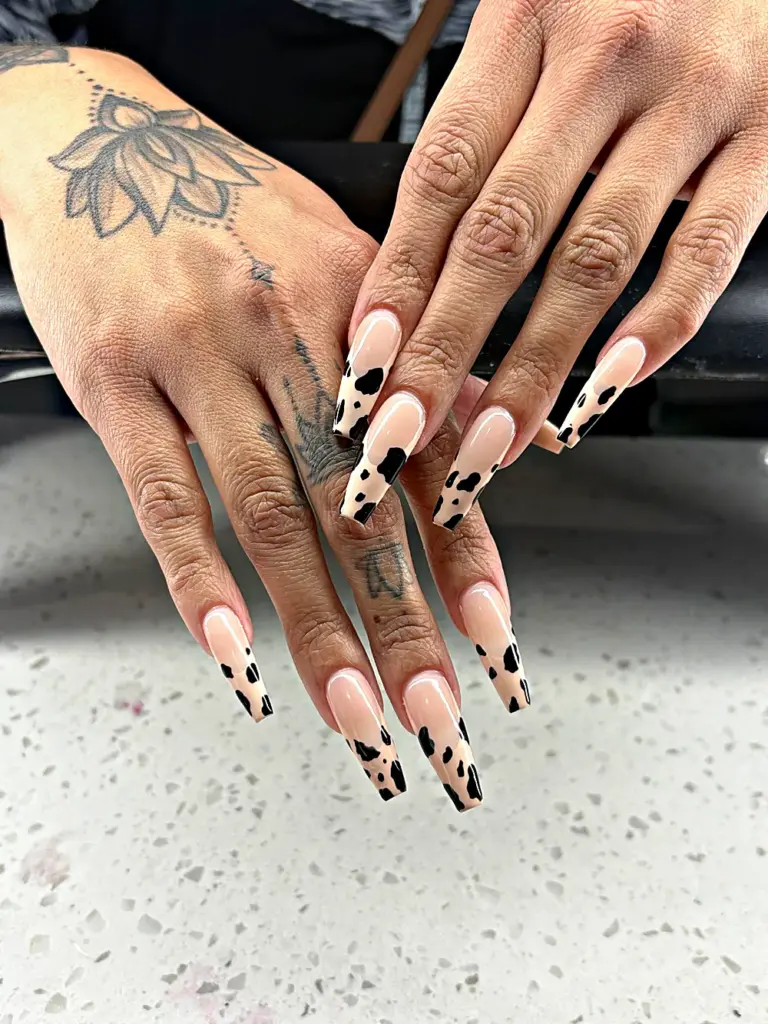 Long coffin Gel X nails with a nude base and black and cream cow print tips at NAB Nail Bar in Las Vegas