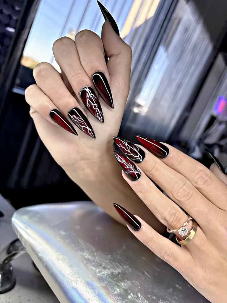 Long stiletto Gel X nails in burgundy and black with hand-painted white lightning at NAB Nail Bar in Las Vegas