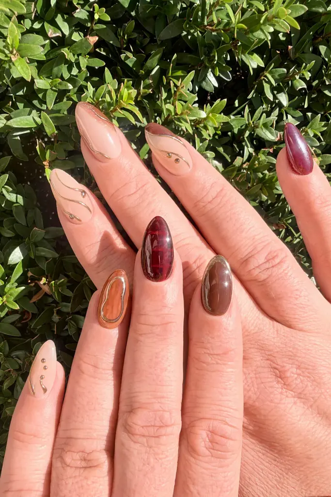 Medium almond Gel X nails in brown, wine and nude with gold chrome wire and studs at NAB Nail Bar in Las Vegas
