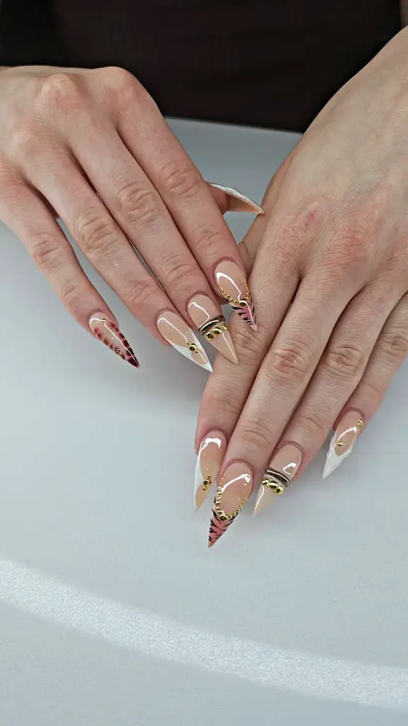 Medium stiletto Gel X nails in nude with tiger print, white French and gold studs at NAB Nail Bar in Las Vegas