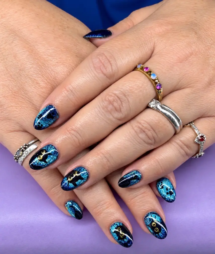Short oval Gel X nails in blue cat eye with black cats and gold charms at NAB Nail Bar in Las Vegas