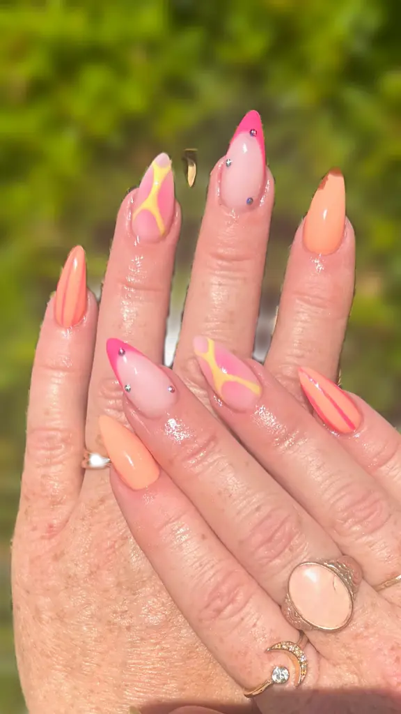 Short stiletto Gel X nails in peach orange with hot pink French tips and yellow abstract lines at NAB Nail Bar in Las Vegas
