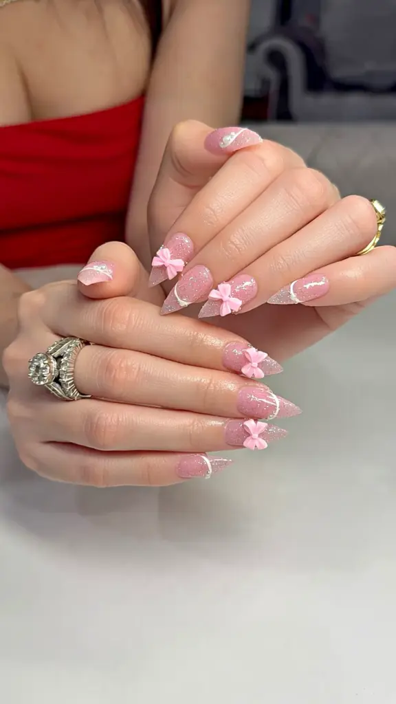 Short stiletto Gel X nails in pink glitter with 3D pink bows and pearls at NAB Nail Bar in Las Vegas